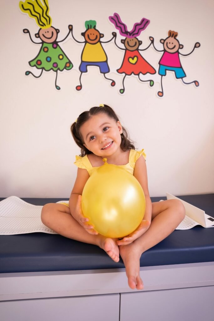 Happy child sitting on medical table holding yellow balloon, smiling.